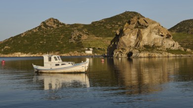 A small boat in the calm water in front of rocks and a small hut on the coast, rocks of Kalikatsou,