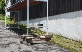 A building with a black wooden facade over a white stone base on a slope, scaffolding in front of