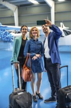 Group of businesspeople taking a selfie with smartphone in hangar before boarding their private jet