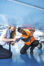 Aircraft maintenance engineer and pilot working together, inspecting the underside of an airplane