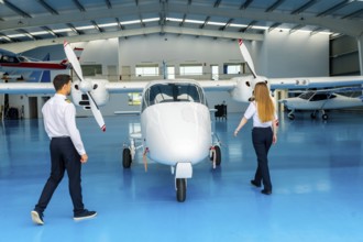 Two pilots walking around a small airplane inside an aircraft hangar, preparing for pre flight