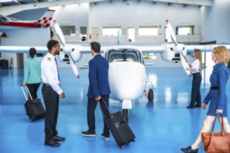 Business people walking towards a private jet with their luggage, accompanied by the pilot and crew