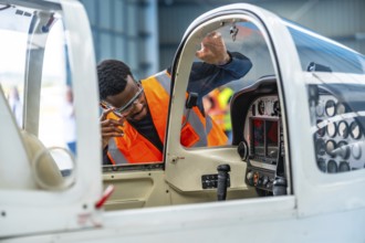 Aircraft engineer wearing safety glasses and a high visibility vest inspects the cockpit of a small