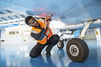 African american aviation technician wearing safety glasses and vest inspecting aircraft wing in