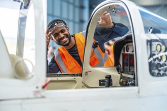 Smiling aircraft maintenance engineer waving from the cockpit of a small plane during pre flight