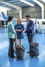 Businesspeople are talking and smiling in an aircraft hangar with their luggage near a private jet
