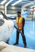 Aircraft maintenance engineer wearing a high visibility vest carefully inspects the propeller of a