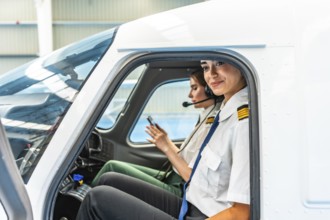 Two female pilots sitting inside the cockpit of a small airplane, preparing for take off and