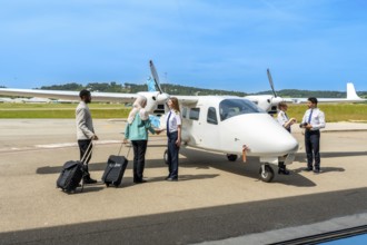 Passengers with luggage shaking hands with female pilot before boarding small private airplane on