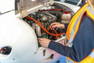 Aircraft mechanic wearing high visibility vest working on airplane engine during maintenance check