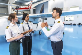 Flight instructor conducting a training session with two pilots inside an aircraft hangar,