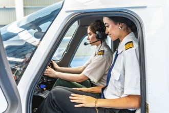 Two female pilots sitting inside the cockpit of a small airplane, preparing for take off, wearing