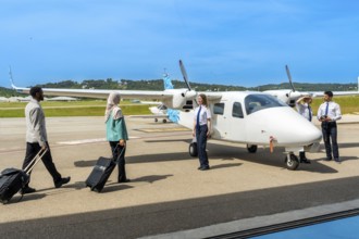 Passengers carrying trolley bags walking towards small airplane and flight crew, ready for boarding