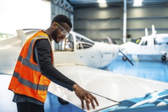 Aircraft maintenance engineer wearing safety glasses and a high visibility vest checks the wing of