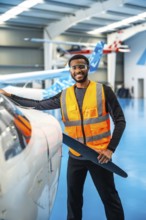 Smiling african american aviation engineer holding a propeller blade, performing maintenance checks