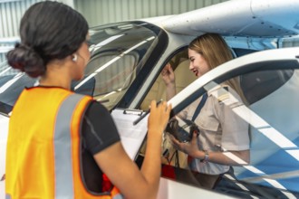 Aircraft maintenance supervisor holding checklist, talking with female pilot sitting in cockpit,