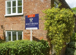 Mortimers estate agent 'Sold' sign outside red brick house, Shottisham, Suffolk, England, UK