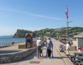 Two elderly people walking with rollators, Seafront promenade view west towards Teignmouth, south