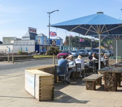People sitting outside cafe near seafront on sunny day, Teignmouth, south Devon, England, UK