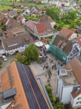 Aerial view of a village square with people and traditional buildings with tiled roofs, family