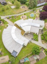 Modern architecture in a U-shaped building with surrounding greenery and playground facilities seen