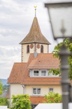 Tower of a church with clock, surrounded by buildings with red roofs and a cloudy sky, family