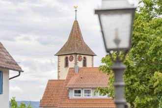Idyllic view of a church tower with weathercock in the village with blue sky and clouds, family