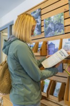 Woman in leisure look reads a brochure in an information centre with wooden shelves, family