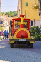 Colourful tourist train runs through a busy street full of people and decorations, Calw station