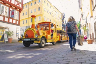 A colourful train runs through a sunny, lively city street, Calw station festival, Black Forest,