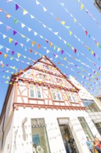 Half-timbered house decorated with colourful flags under a blue sky, Calw station festival, Black