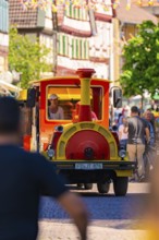 Colourful procession drives through a lively old town street, surrounded by passers-by, Calw