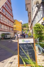 Half-timbered house street with board and bicycle in the foreground, sunny cityscape, Calw railway