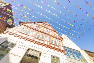 Medieval half-timbered house with colourful pennants in front of a blue sky, Calw station festival,