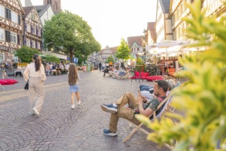 People relaxing on a lively old town square surrounded by historic buildings, Calw railway station