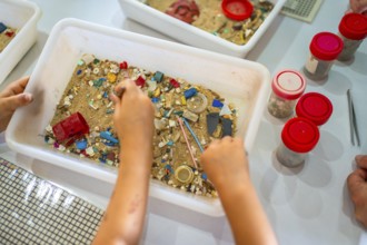 Students using tweezers collecting colorful microplastics from sand in a white plastic container