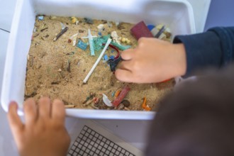 Young student analyzing a sand sample containing microplastics, highlighting the growing concern of
