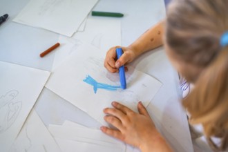 Young girl concentrating intently while drawing with a blue wax crayon on crisp white paper at her