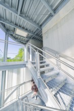 A woman on a modern metal staircase in a light-flooded interior, Zob extension with bridge