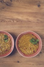Two bowls of barley stew sit on a wooden table, each garnished with green herbs, capturing the