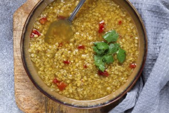 A hearty bowl of lentil soup garnished with fresh herbs sits on a wooden board. The warm colors and