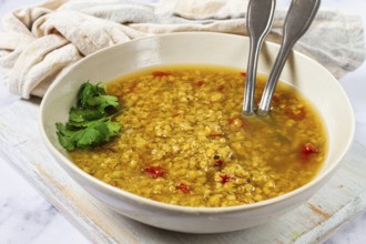 A warm lentil soup with a rich golden color is served in a rustic bowl. The soup features fresh