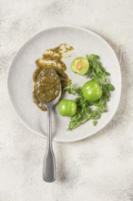 A spoon with tkemali sauce, on a plate, with cherry plum and mint, top view, no people