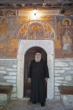 Greek Orthodox priest standing by murals from 1802, Agia Marina church, Kissos, Pelion peninsula,