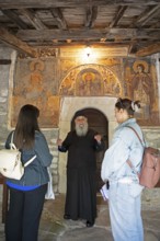 Greek Orthodox priest explains wall paintings from 1802 to visitors, Agia Marina church, Kissos,