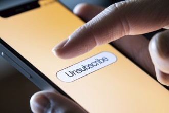 Person's finger hovering over unsubscribe button on mobile phone screen. Generative Ai, AI