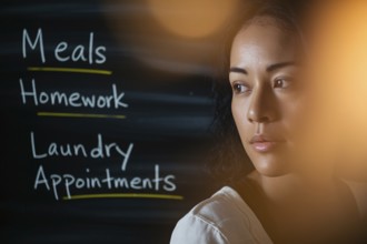 Thoughtful woman in warm light with task-filled blackboard. Concept of mental load, emotional