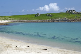 Pristine sandy beach with clear turquoise water and green hill in the background, St Agnes, Isles