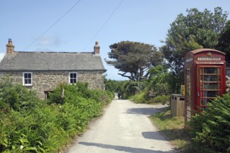 A rural scene with a stone house and red brtish telephone box along a narrow path under a blue sky,
