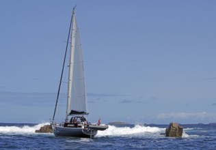A sailing boat on the open sea, surrounded by rocks and waves, under a clear sky, St Agnes, Isles